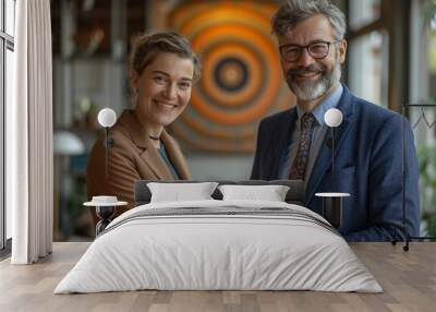 A smiling young woman and an older man shake hands, symbolizing partnership. The modern workspace reflects collaboration and success. Wall mural