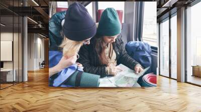 Two girlfriends traveler with backpacks and inventory go in the train and watch the further route on the map Wall mural