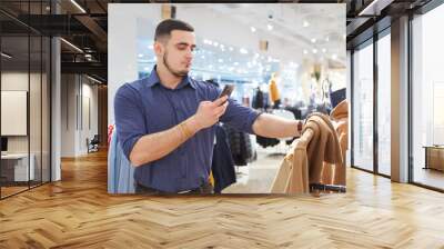 Young man scans a qr code using a smartphone in a clothing store Wall mural