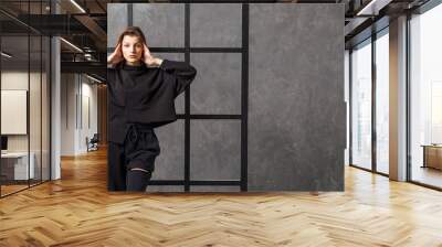 Young woman in black sportswear, pants and sweatshirt. Concept of fashionable sport outfit, indoors photo. Copy space. Wall mural