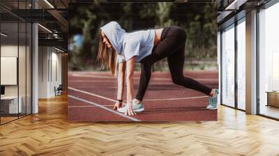 Ready to go! Female athlete on the starting line of a stadium track, preparing for a run. Fitness girl is preparing to run from a low start. Healthy lifestyle. Wall mural