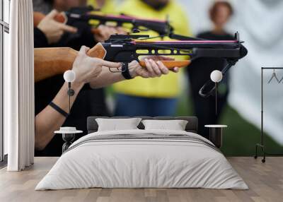 girl shoots from a crossbow close-up. A young girl is aiming at a target with a crossbow. girl shoots from a crossbow in a summer outdoor shooting range. Wall mural