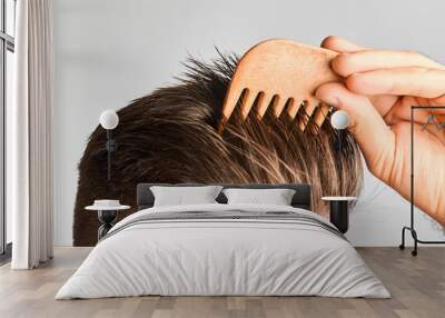 Young man styling his hair with a wooden comb. Hair styling at home. Advertising concept of shampoo for healthy hair and against dandruff.  Wall mural