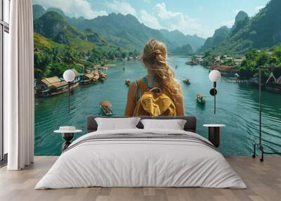 
a girl with a backpack standing on a bridge and looking at the river with boats and mountains in the background Wall mural