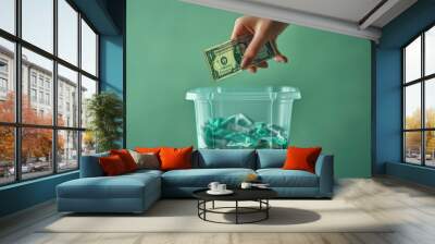 A hand discards a dollar bill into a clear container filled with green wrappers, symbolizing waste and lost value in a minimalistic setting Wall mural