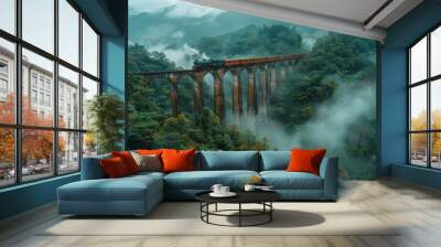 A vintage steam train crosses a historic viaduct surrounded by misty mountains and lush greenery early in the morning Wall mural