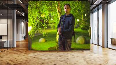 A guy stands against the background of a green birch tree at night in the park	
 Wall mural