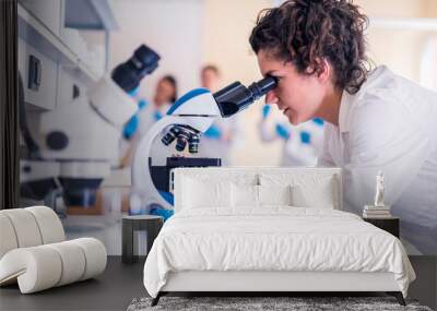 Young female scientist looking through a microscope in a laboratory doing research on finding medicine pharmacy cure vaccine  Wall mural