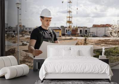 builder in helmet and with a drawing on the background of a house under construction Wall mural