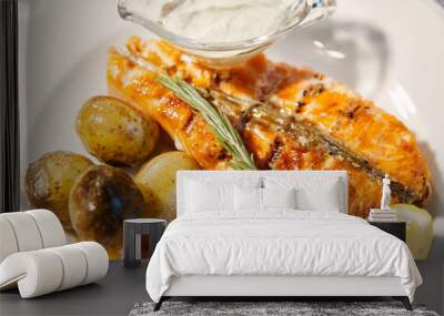 Grilled fish is on white plate with potatoes, lemon and sauce, Thyme branch, close up Wall mural