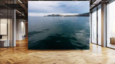 Beautiful view of the water of Lake Baikal per day with clouds in the sky. View from the water. The water is green. On the horizon are hills. Wall mural