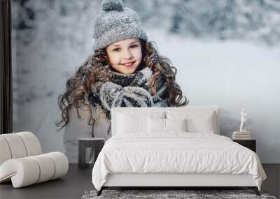 Little girl in a gray jacket, catches snowflakes in a winter park. Children play outdoors in a snow-covered forest. Children catch snow flakes. Wall mural