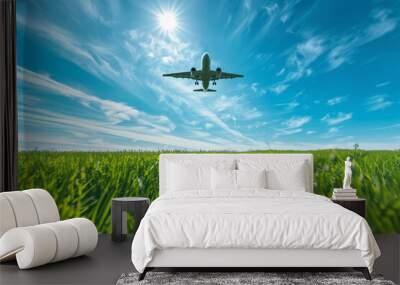 Low Angle View of Flying Airplane Over Green Field. Commercial airplane flying low over a lush green field on a sunny day, ideal for travel and tourism themes. Wall mural