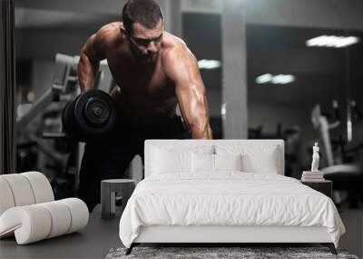 Man trains in the gym. Athletic man trains with dumbbells, pumping his biceps Wall mural