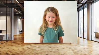 portrait of a happy child on a white background in a green t-shirt smiling. The little girl plays with her sly eyes. Happy girl. copy space. Childhood concept. Wall mural