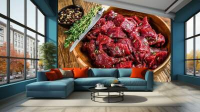 Raw cut wild venison meat for a goulash in a wooden plate. Wooden background. Top view Wall mural