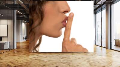 Cropped image of a young woman holding index finger at her lips, saying 'shh' on a white background. side profile view Wall mural