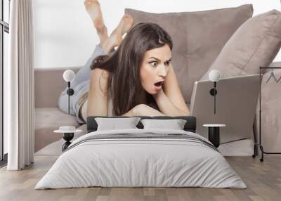 shocked girl lying on the couch and working on her laptop Wall mural