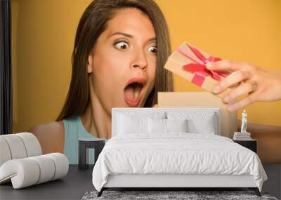 Young shocked woman opening a present box on yellow background Wall mural