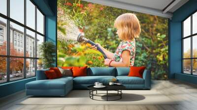 Cute little girl watering flowers with a hose in the garden Wall mural