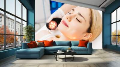 A cosmetologist performs LED light therapy for facial rejuvenation. This non-invasive treatment improves skin elasticity, reduces aging signs, and enhances overall skin radiance. Wall mural