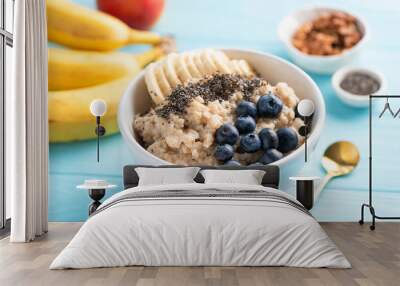 Oatmeal porridge with banana, blueberries and chia seeds in white bowl on blue background. Healthy breakfast food Wall mural