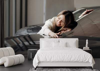 
smiling beautiful woman hugging her new car in a car dealership. young woman fulfills her dream, lies on the car. Wall mural