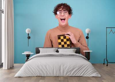 Mind games. An attractive guy in a brown sweater poses with chess on a blue background. Wall mural