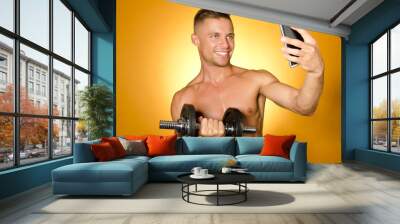 Sexy guy with a dumbbell makes a selfie. Wall mural