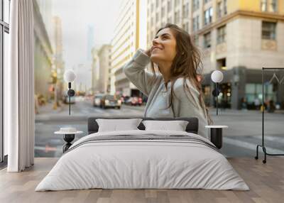 Beautiful young woman on the boulevard in urban scenery, downtown, at sunset, holding smartphone Wall mural