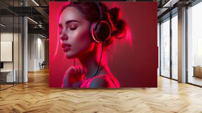 A girl with closed eyes listens to music with headphones on a red background Wall mural