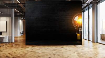 A glowing light bulb against a dark background, symbolizing innovation, creativity, and bright ideas. Wall mural