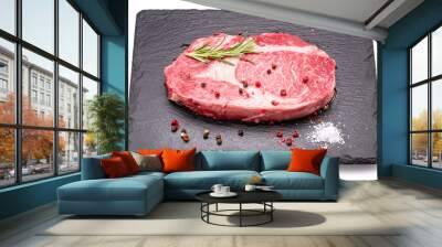 Raw ribeye steak with pepper corns and rosemary on graphite serving board isolated on white background. Wall mural