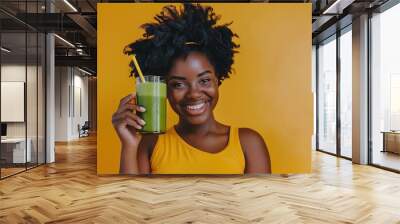 Radiant young woman enjoying a fresh green smoothie against a vibrant yellow background Wall mural