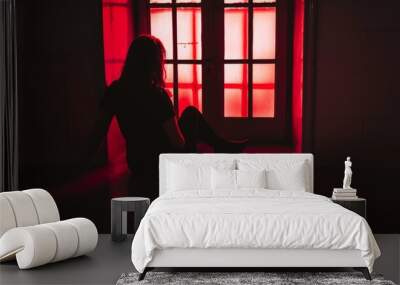 Silhouette of a woman sitting by a window in red light Wall mural