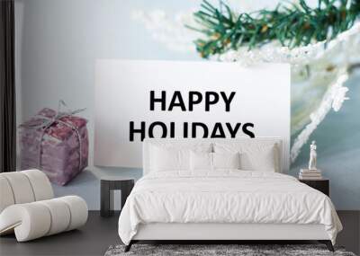 Happy Holidays text on a card next to a gift and spruce branches, festive background Wall mural