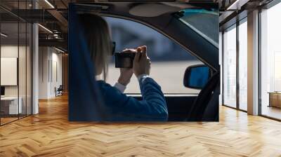 Woman in sunglasses with a camera sits in a car and takes pictures with a professional camera, a private detective or a paparazzi spy. Journalist is looking for sensations and follows celebrities. Wall mural