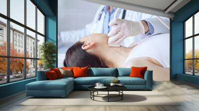 Doctor man is using ultrasound equipment on neck of female patient lying down for a medical examination. Medicine and science Wall mural