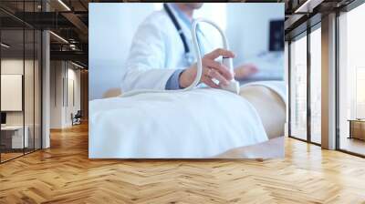 Doctor man wearing a white coat using an ultrasound equipment on a female patient lying down in clinic cabinet. Preventive therapy in medicine Wall mural