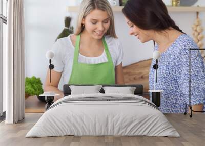 Two young happy woman making cooking in the kitchen. Friendship and culinary concept Wall mural