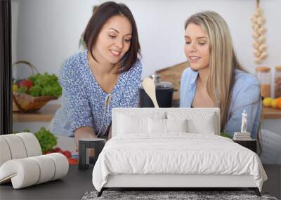 Two young happy women making online shopping for making menu by tablet computer. Friends cooking in the kitchen Wall mural