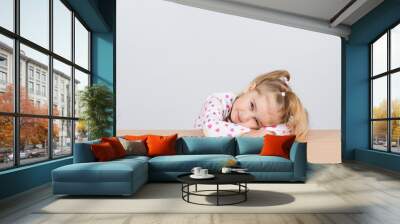  little girl resting head on wooden surface at table. Wall mural