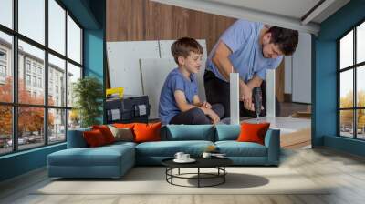 Father and son assemble new furniture on floor of new apartment, concept of experience and training. Wall mural