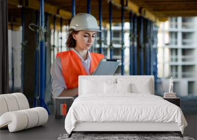 Female construction engineer. Architect with a tablet computer at a construction site. Young Woman looking, building site place on background. Construction concept Wall mural