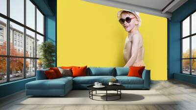 Portrait of a happy boy 6-7 years old in a hat and swimming shorts on a yellow background, sea and summer Wall mural