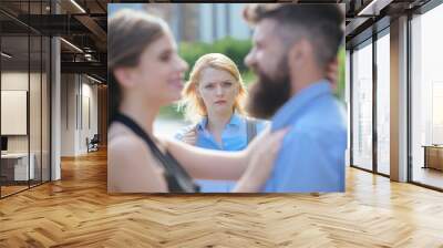 A jealous girlfriend. Unhappy girl feeling jealous. Bearded man cheating his girlfriend with another woman. Romantic couple of man and woman dating. Jealous woman look at couple in love on street Wall mural