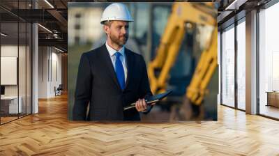 Architect at a construction site. Architect man in suit and helmet at construction site. Confident architect standing at construction. Investor or civil engineer. Outdoor portrait of hispanic Wall mural