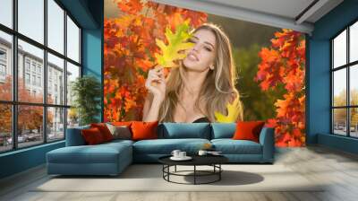 Beautiful girl outdoors in autumn fall. Young woman collects yellow fall leaves in autumn. Beauty woman holds autumn yellow leaf fall the face. Portrait of sensual woman over autumn fall background. Wall mural