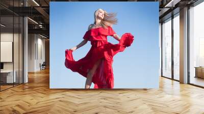 Blonde woman in red dress movement on sky. Fashionable young model in style dress. Fashion woman in summer. Wall mural