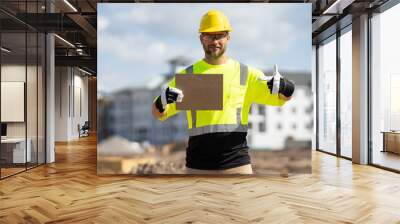 Builder in a hard hat working on a construction project at a site. A builder worker in a helmet near building construction sites. Builder on the job. Man worker in builders helmet on the building site Wall mural